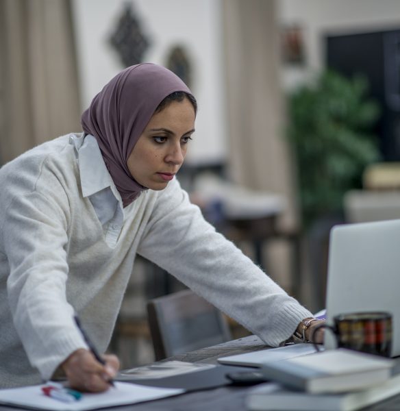 Photo d'une femme portant un hijab et une blouse de laboratoire, debout devant un ordinateur portable.